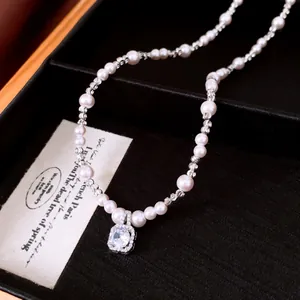 Detailopname van een parelketting met vierkante zirkoon hanger in een juwelendoos.