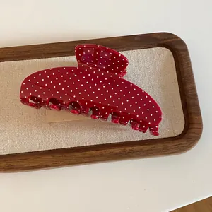 Detailopname van een rode acryl haarklem met witte stippen op een houten dienblad