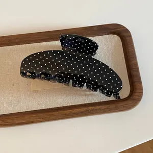 Detailweergave van de zwarte acryl haarklem met een klassiek wit stippenpatroon.