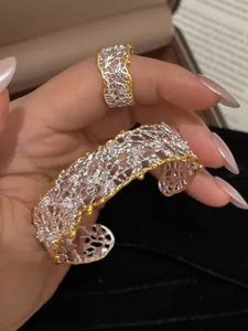 Primo piano di un bracciale rigido vintage traforato bicolore con anello coordinato.