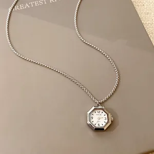 Gros plan d'un collier pendentif montre octogonal avec chaîne argentée sur fond taupe