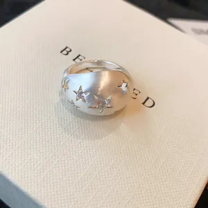 Detailopname van een matte zilveren ring met steruitsparingen en zirkonia steentjes.