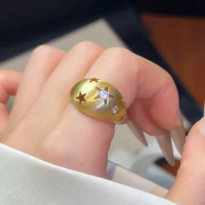 Detailopname van een geborstelde gouden ring met sterren en fonkelende zirkonia stenen.