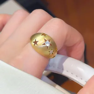 Close-up van goud geborstelde metalen ring met opengewerkte sterpatronen en zirkoon.