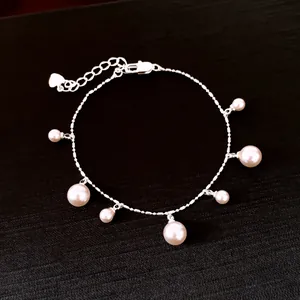 Detail view of silver chain bracelet with dangling white pearls on black background
