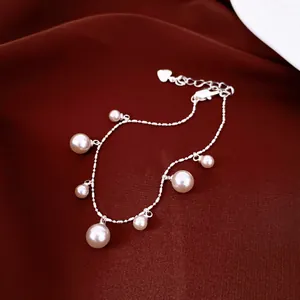 Elegant silver-tone chain bracelet featuring dangling pearls on a red silk background