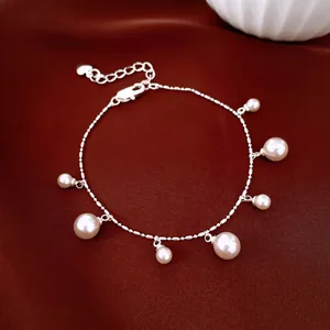 Detailed shot of a silver chain bracelet featuring dangling white pearls on luxury red silk background.