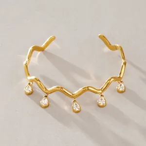Detailansicht eines goldenen gewellten Edelstahl-Armreifs mit Zirkonia-Anhängern.