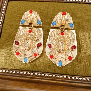 Detaillierte Nahaufnahme ägyptischer Skarabäus-Ohrringe in Gold mit bunten Steinen.