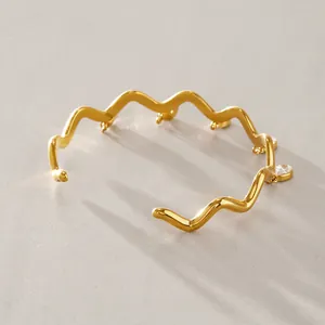 Detailansicht eines goldenen gewellten Armreifs aus Titanstahl mit Zirkonia-Anhängern.