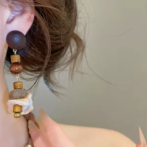 Detailed view of retro shell and wooden bead drop earrings worn by a female model