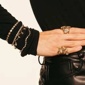 Detailansicht von goldfarbenen Wellenarmbändern und Ringen mit Zirkonia-Anhängern.