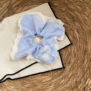 Detailopname van een blauwe ruitjes scrunchie met witte kant en een hartstrikje