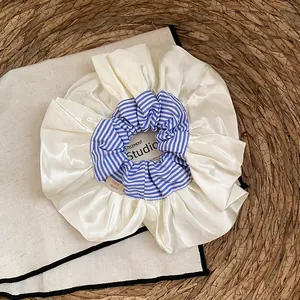 Detail van een grote crèmekleurige satijnen scrunchie met blauw gestreepte rand