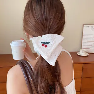 Achteraanzicht van een witte kanten scrunchie met kersenborduurwerk op bruin haar