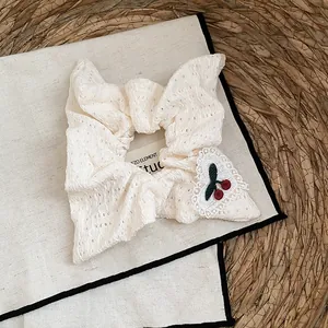 Detail van een crème kanten haarelastiekje met een schattig geborduurd kersenhart