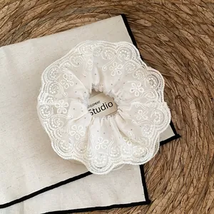Detail van een elegante gebroken witte kanten scrunchie met fijn bloemenborduurwerk