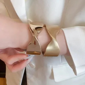 Detail view of two gold-toned pleated cuff bracelets with glossy and matte finishes
