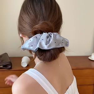Mooie zilveren satijnen scrunchie met zwarte stippen op een stijlvol knotkapsel.