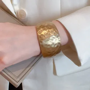 Detailed view of a golden textured wide open cuff bangle on a wrist paired with a white blazer