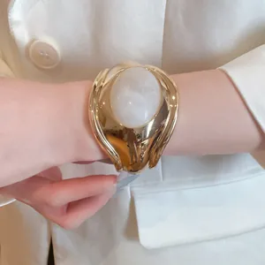 Close-up of gold pleated cuff bracelet with large white oval resin inlay