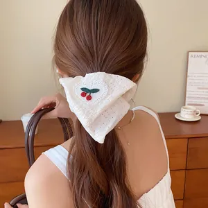 Gedetailleerd beeld van een witte kanten scrunchie met zoet kersenborduurwerk.