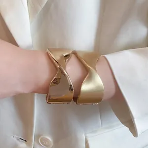 Detail view of two gold-finish pleated bangles showing polished and matte textures