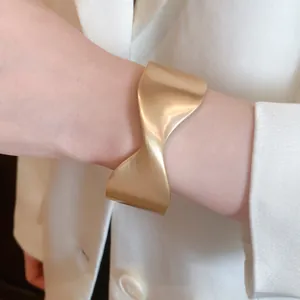 Detailed macro view of a stylish matte gold twisted resin cuff bracelet on wrist.