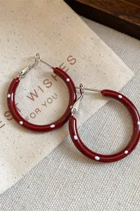 Close-up detail of red enamel hoop earrings with white polka dots and silver needle