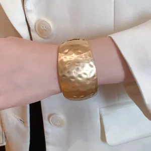 Detail showing the hammered texture of a gold-toned wide open cuff bracelet on a wrist