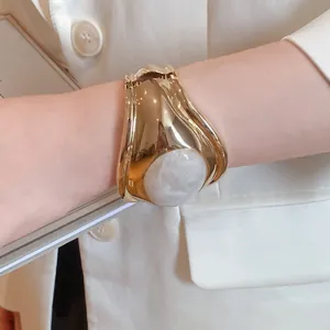Detailed view of wide gold cuff bracelet with white marble-like resin oval stone