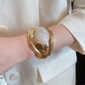 Close-up of a bold gold-tone pleated cuff bracelet with a large white oval resin stone.
