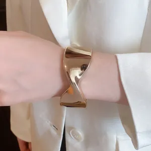 Close-up of a minimalist gold twisted cuff bracelet styled with a professional white blazer