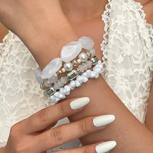 Primo piano di un set di quattro braccialetti bianchi con perline in acrilico e vetro.
