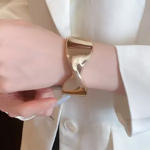 Macro detail of a high-shine gold twisted cuff bracelet styled on a wrist with a white blazer