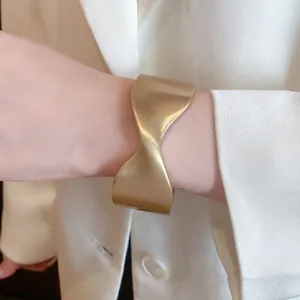 Detailed close-up of wide gold sculptural cuff bracelet with a matte brushed finish