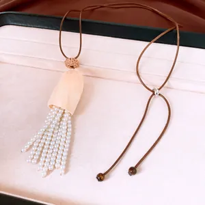 Detail of handmade necklace with white pearl tassel and light wood shell pendant