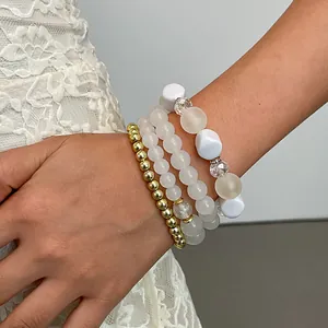 Dettaglio di un set di quattro braccialetti vintage con perle bianche e oro su un polso