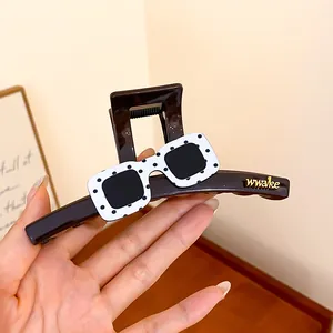 Dettaglio di una pinza per capelli marrone con occhiali a pois e accenti dorati del logo.