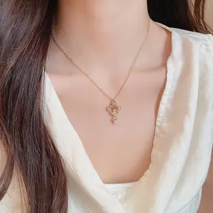 Détail en gros plan d'un collier cœur et fleur de lys plaqué or 14K sur un modèle