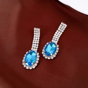 Elegante Tropfenohrringe mit ovalen blauen Edelsteinen und funkelnden Strasssteinen auf Seide.