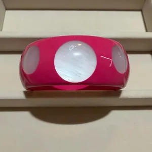 Bright pink wide bangle with white round shell-like inlays on a jewelry display tray.