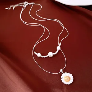 Detail view of a silver-tone necklace with pearls and a delicate white daisy pendant.