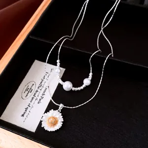Close-up detail of a silver daisy pendant necklace with elegant white pearls inside a box