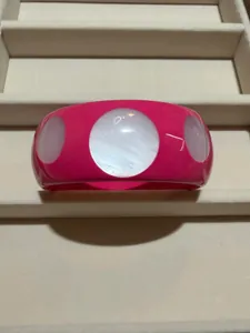 Detail view of a fuchsia resin bangle featuring large white shell-like circular inlays.