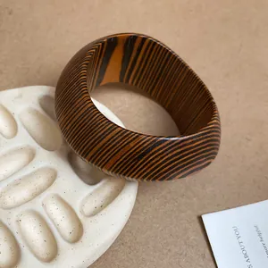 Close-up of a wide wooden bangle with natural brown striped pattern and polished finish