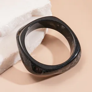 Close-up detail of a modern black marbled square bangle bracelet resting on white stones