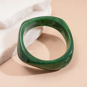 Close-up of a chunky green marbled resin bangle with a unique curved square design.
