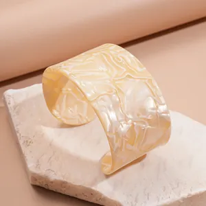 Close-up detail of a cream marbled wide cuff bracelet displayed on a natural stone base