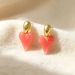 Macro view of pink resin heart stud earrings displayed on soft off-white textured fabric